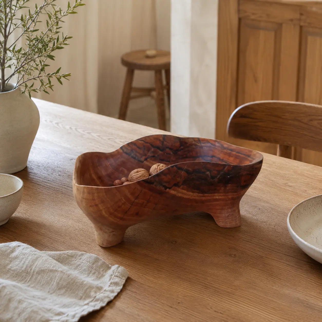 Sculptural wooden bowl on short carved legs displayed as an editorial focal point in a calm kitchen interior.